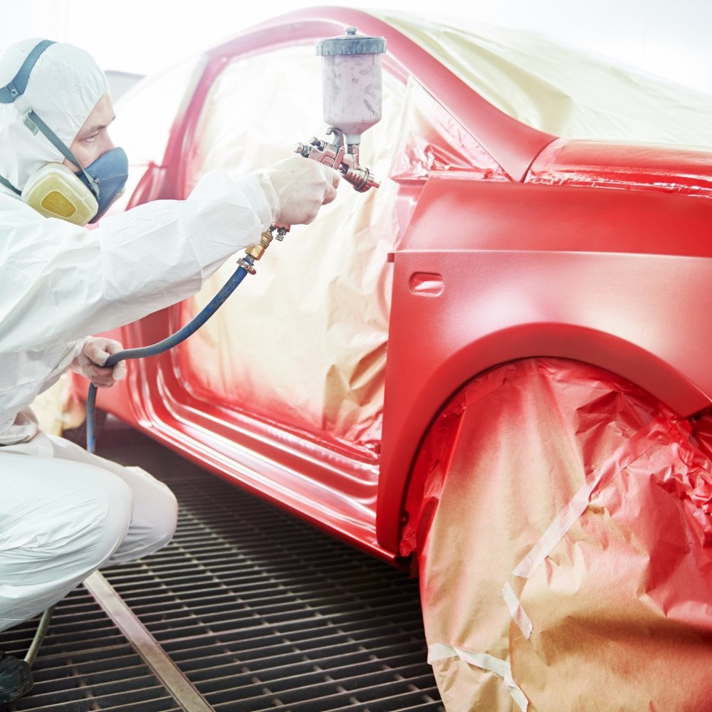Painter spraying a masked body panel in a spray booth